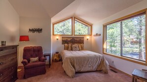 Un dormitorio con una cama grande, una lámpara roja, un aparador de madera y una ventana con vistas a árboles.