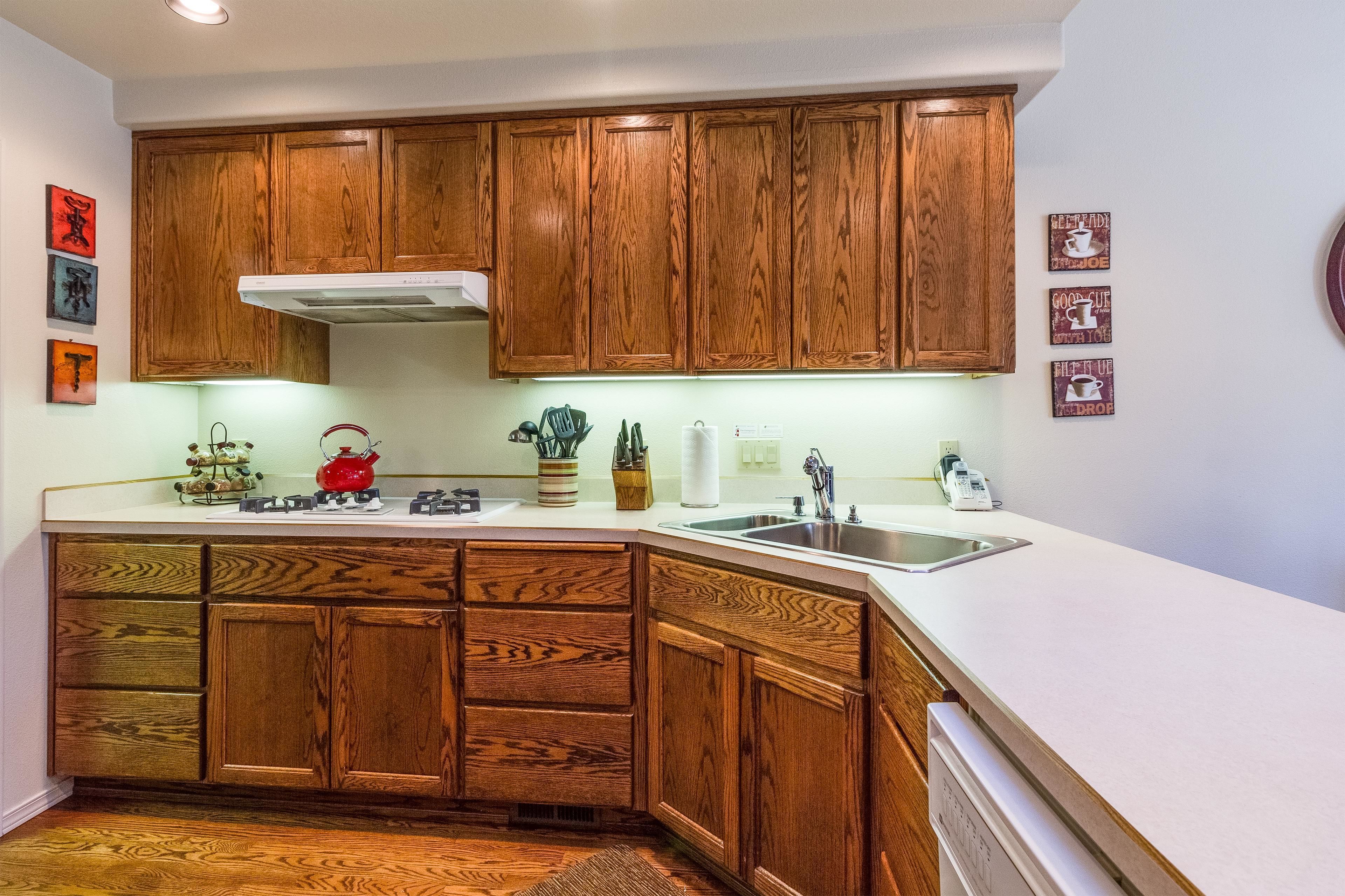 A kitchen with wooden cabinets, a white countertop, a stove, and a sink.