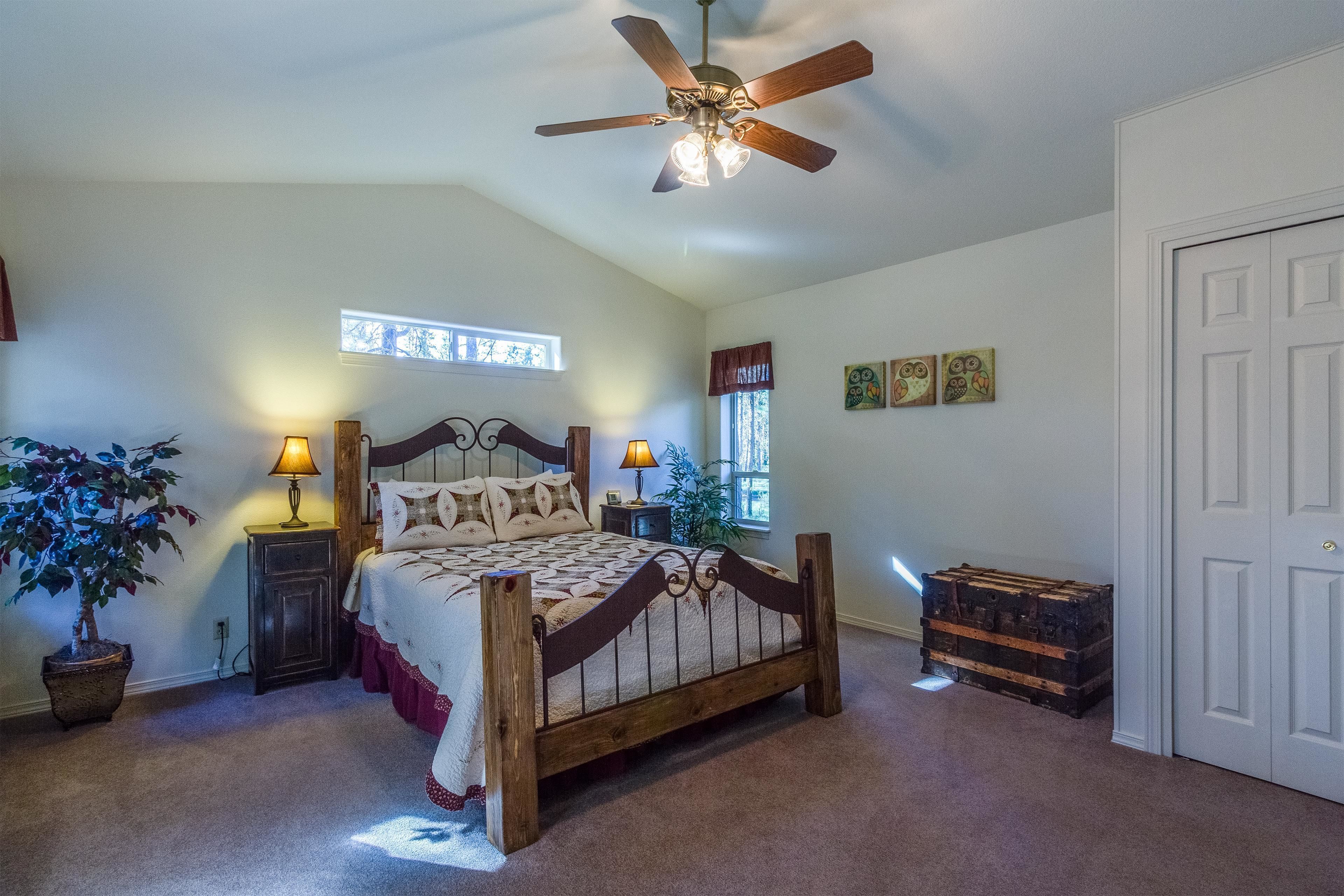 A bedroom with a wooden bed, two bedside lamps, a ceiling fan, a window with curtains, and a door.