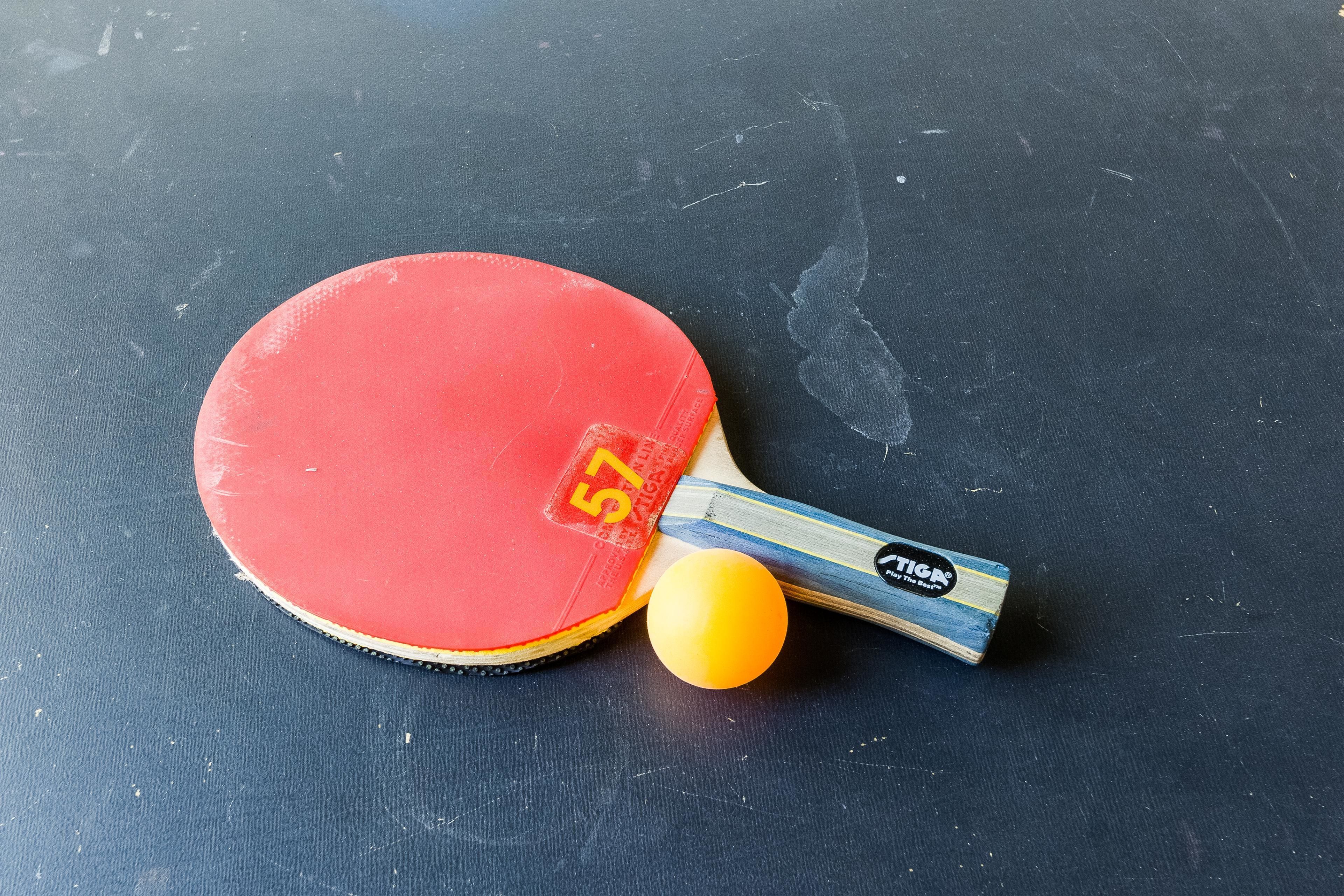 A table tennis table with a red paddle and a yellow ball.