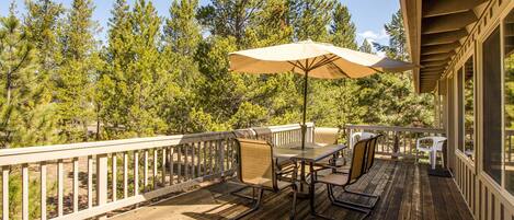 A wooden deck with outdoor furniture, including a table and chairs, and a large umbrella providing shade.