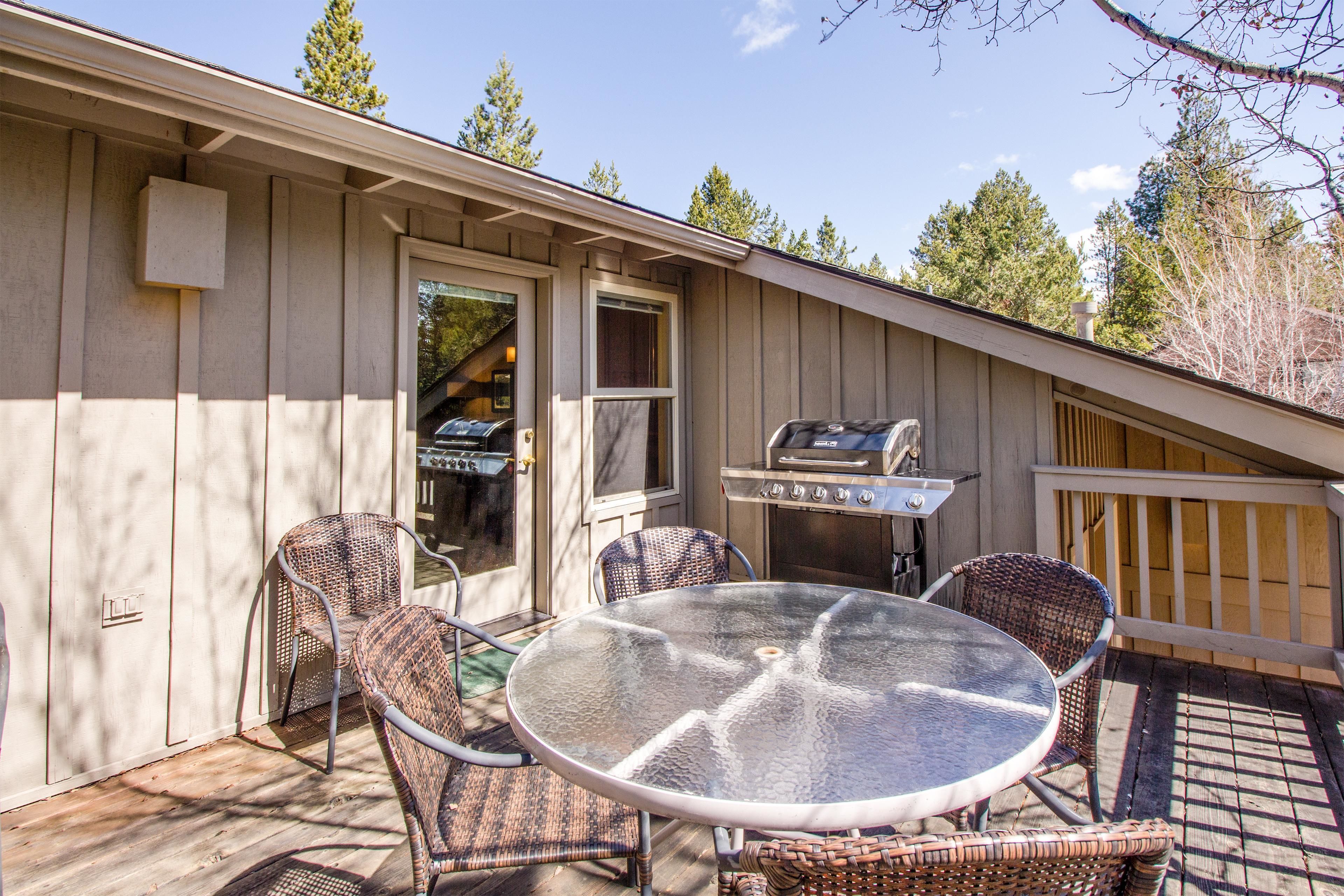 A covered patio with a glass table and wicker chairs, a grill, and a wooden deck.