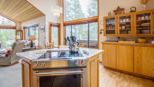 A modern kitchen with a central island, wooden cabinets, and large windows offering views of trees. - Red Alder 3 (Bend)