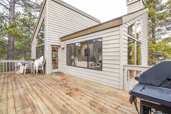 A wooden deck with outdoor furniture, a grill, and a large window overlooking the deck.