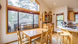 A kitchen with a wooden table and chairs, a window with a view of the outside, and wooden cabinets. - Red Alder 3 (Bend)