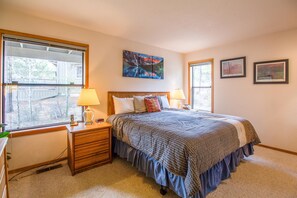 A bedroom with a large bed, two bedside lamps, a wooden nightstand, and a window with a view of trees.