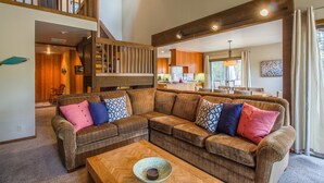 A spacious living room with a large sectional sofa, wooden staircase, and a kitchen in the background. - Alpine 7 (Bend)