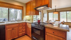 A modern kitchen with wooden cabinets, a stainless steel stove, and large windows offering views of the outdoors. - Alpine 7 (Bend)