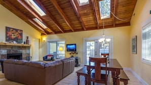 A spacious living area with a large brown leather sofa, a wooden dining table with four chairs, a fireplace, and a television.
