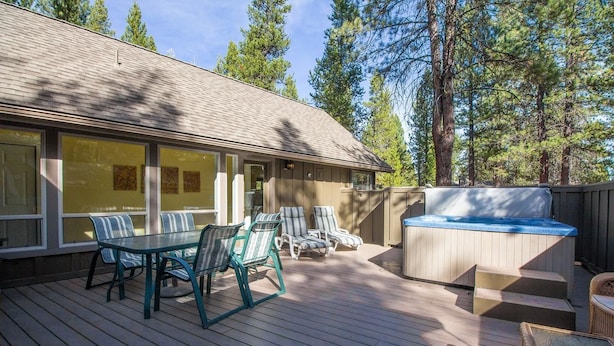A covered deck with outdoor furniture, a hot tub, and a view of a forested area.