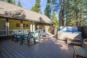 A covered deck with outdoor furniture, a hot tub, and a view of a forested area.