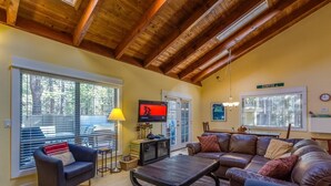 A cozy living room with a wooden ceiling, a television, a dining area, and large windows.