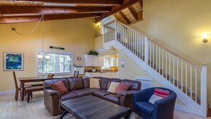 A spacious living room with a brown leather sectional sofa, a blue armchair, and a wooden coffee table. A staircase with a white railing leads to an upper level.