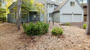 A two-story house with a garage, surrounded by trees and a gravel driveway. - Siskin 12 (Bend)