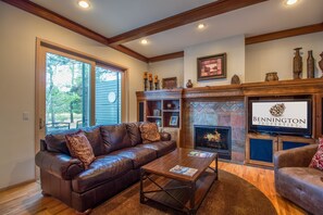 A living room with a leather sofa, coffee table, fireplace, and wooden beams on the ceiling. - Siskin 12 (Bend)