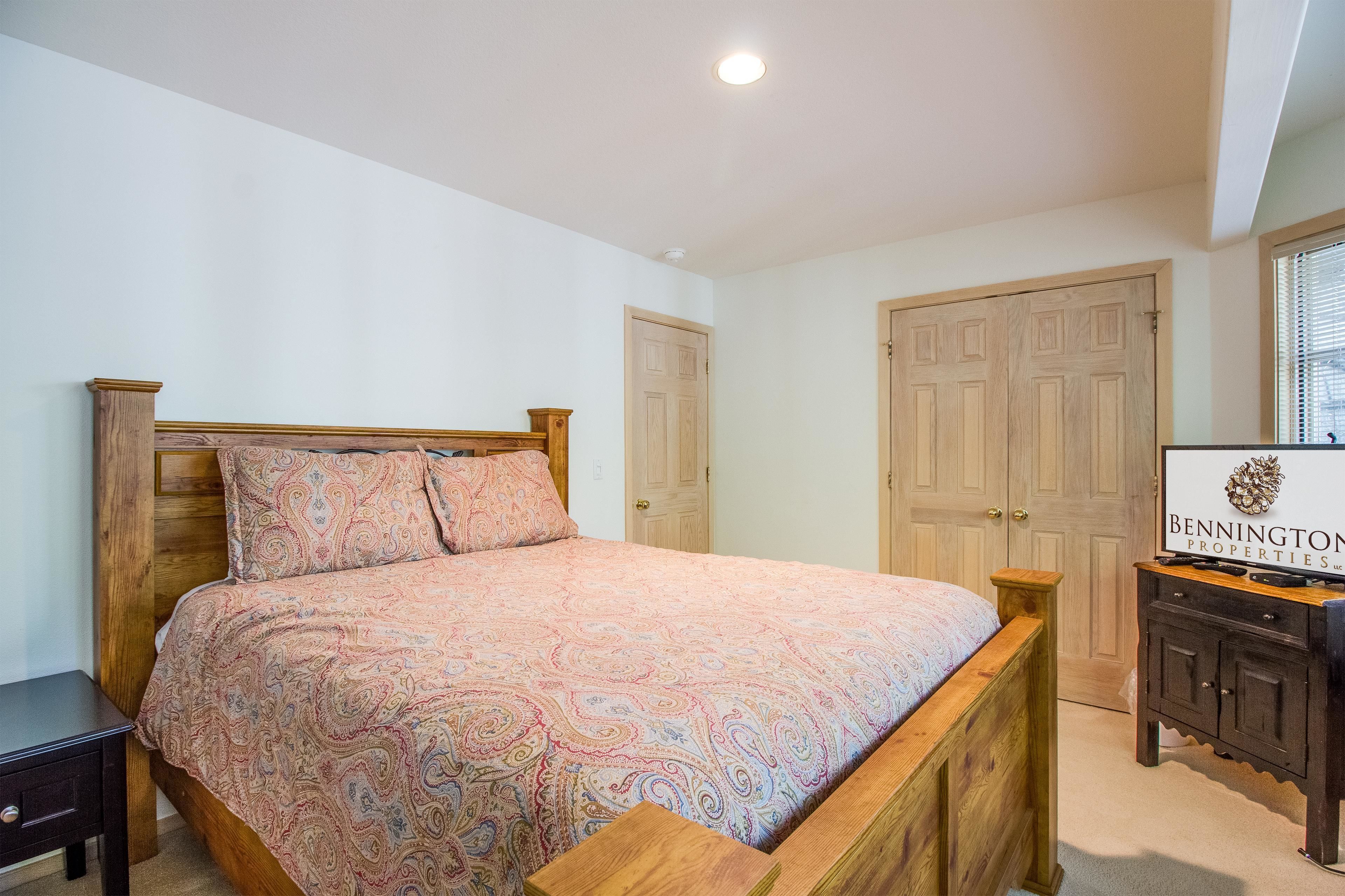 A bedroom with a wooden bed, a nightstand, a dresser, and a sign for Bennington Properties Inc.