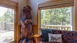 A wooden bear sculpture in a room with a sofa and a view of trees through large windows. - Tokatee 30 (Bend)