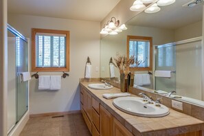A bathroom with two sinks, a large mirror, and a window with blinds. - Tokatee 30 (Bend)