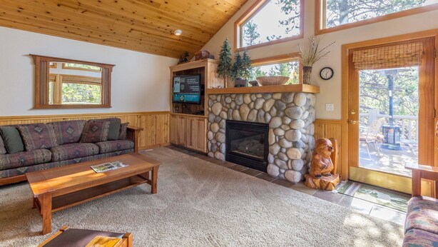 A cozy living room with a stone fireplace, a wooden ceiling, and large windows. - Tokatee 30 (Bend)