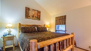 Un dormitorio con estructura de cama de madera, una mesita de noche con lámpara y una ventana con vistas al exterior.