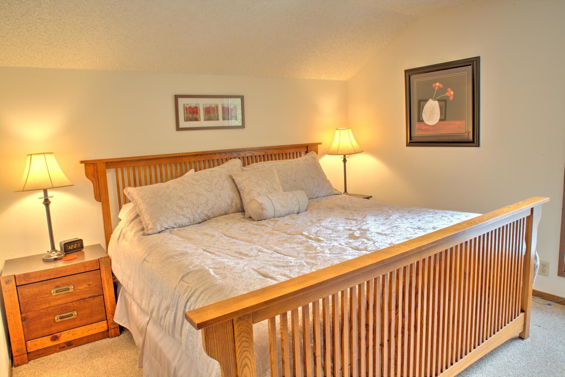 A neatly made bed with a wooden headboard, two bedside tables with lamps, and a framed picture on the wall.