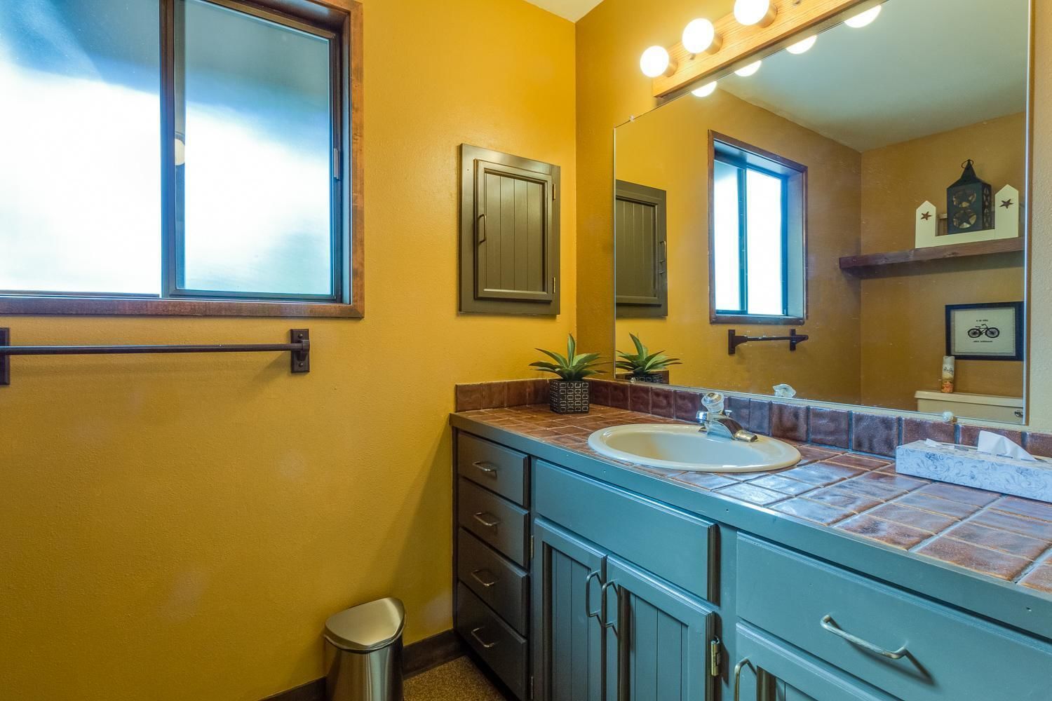 A bathroom with a yellow wall, a sink, a mirror, and a window.