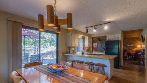 Una cocina moderna con una isla central, un comedor con mesa y sillas de madera, y vistas al exterior a través de grandes puertas correderas.