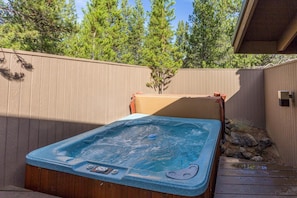 Un jacuzzi en un área de terraza de madera, con una valla de madera y árboles al fondo.