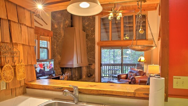 A kitchen with a sink, wooden counter, stone wall, and a large window overlooking a deck.