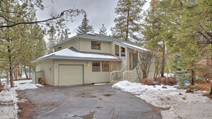 Une maison à deux étages avec un garage, entourée d’un paysage enneigé et d’arbres.