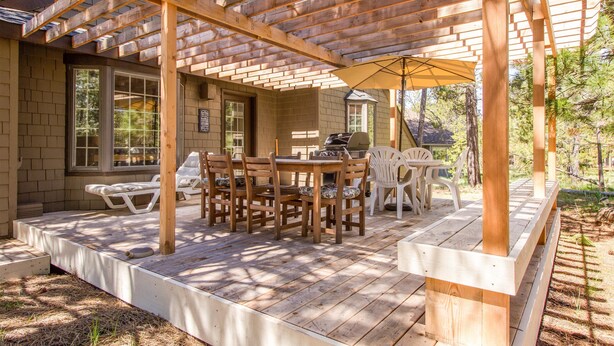 A covered patio with wooden furniture, including a table and chairs, and a grill. - Kinglet 23 (Bend)
