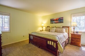 A bedroom with a wooden bed, two bedside tables with lamps, a painting on the wall, and a window on the left. - Kinglet 23 (Bend)
