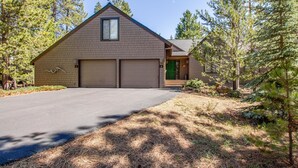 A two-story house with a garage, surrounded by pine trees. - Kinglet 23 (Bend)