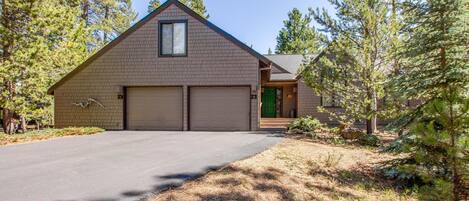 A two-story house with a garage, surrounded by pine trees.