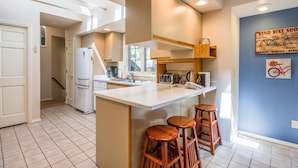 A modern kitchen with a central island, wooden stools, a refrigerator, a microwave, and a coffee maker. - Kinglet 23 (Bend)