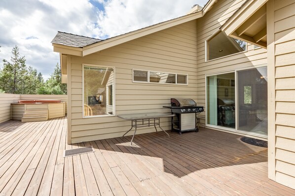 A deck with a grill and hot tub, large windows, and a covered patio area. - Red Wing 11 (Bend)