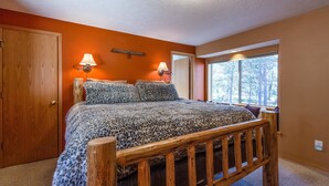 Un dormitorio con cama de madera, dos lámparas fijadas a la pared, una ventana con vistas a árboles y una pared naranja.