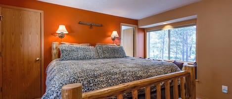 Ein Schlafzimmer mit einem hölzernen Bett, zwei Wandlampen, einem Fenster mit Blick auf Bäume und einer orangefarbenen Wand.