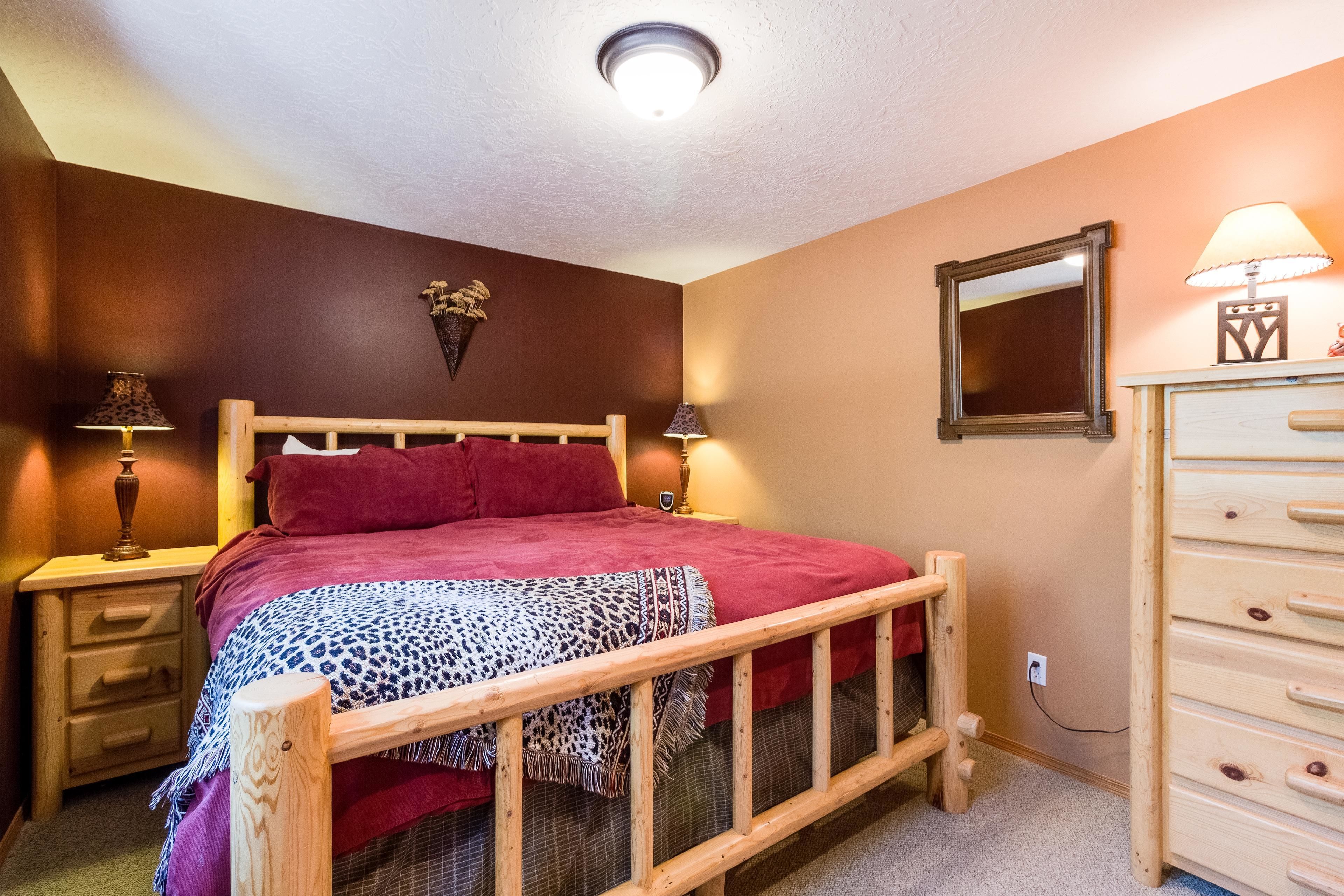 A bedroom with a wooden bed, two bedside tables with lamps, a dresser, and a mirror on the wall.