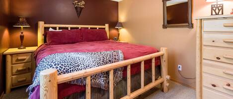 A bedroom with a wooden bed, two bedside tables with lamps, a dresser, and a mirror on the wall.