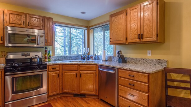 Una cocina con armarios de madera, electrodomésticos de acero inoxidable, encimeras de granito y ventanas amplias.
