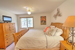 Quarto com cama, penteadeira de madeira, televisão, janela e obras de arte.