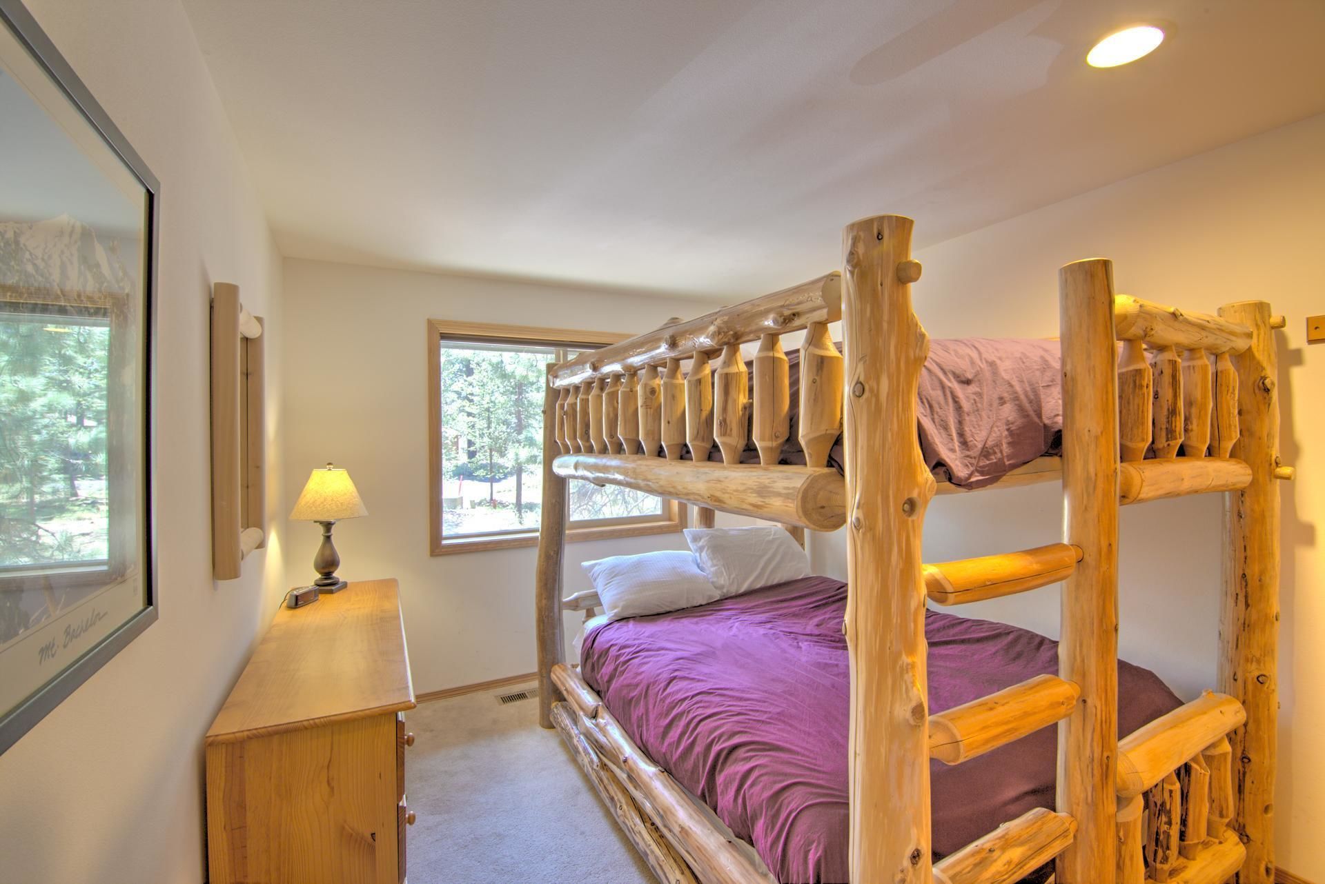 Une chambre avec un lit superposé, une fenêtre, une table de chevet avec une lampe et un tableau encadré au mur.