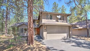 A two-story house with a garage, surrounded by pine trees. - Juniper 18 (Bend)