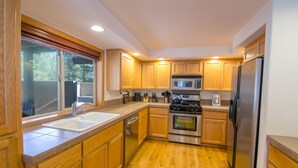 A compact kitchen with wooden cabinets, a stainless steel refrigerator, a microwave, and a stove. - Juniper 18 (Bend)