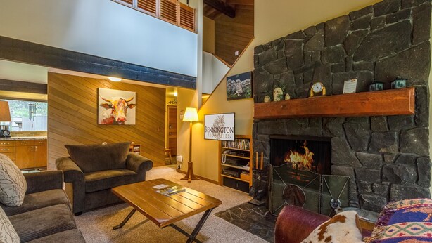 A cozy living room with a stone fireplace, a wooden ceiling, and a comfortable seating area. - Meadow House Cndo 8 (Bend)