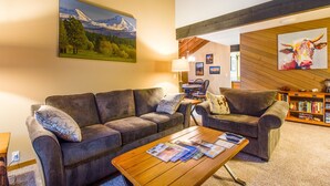 A cozy living room with two sofas, a coffee table with magazines, a bookshelf, and a painting of a mountain landscape. - Meadow House Cndo 8 (Bend)