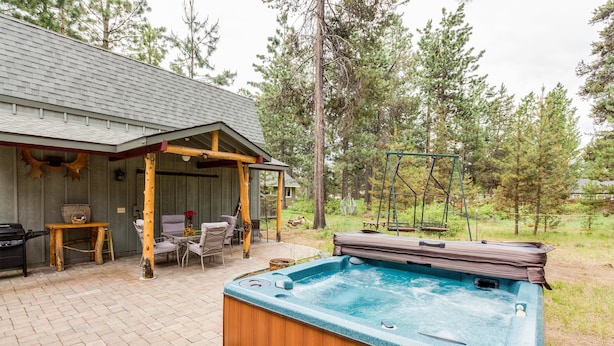 A hot tub in a backyard with a wooden deck, a covered seating area, and a swing set. - Indio Road 16997 (Bend)