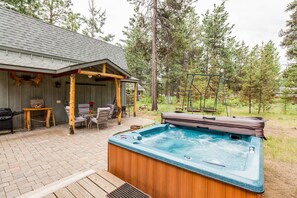 Ein Whirlpool in einem Garten mit einer Holzterrasse, einem überdachten Sitzbereich und einer Schaukel.