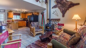 A spacious living area with a fireplace, rustic decor, and a kitchen in the background. - Indio Road 16997 (Bend)